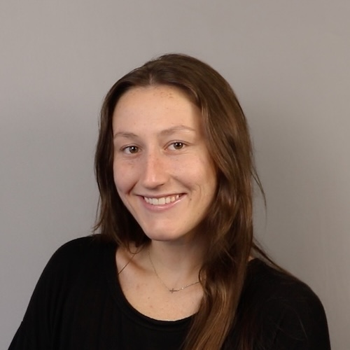 A woman smiling in front of a grey backdrop.