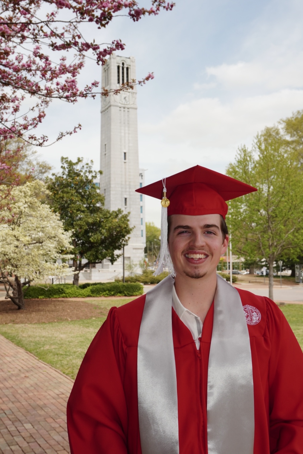 Clark Roberts in his cap and gown standing in front of the NC State Belltower