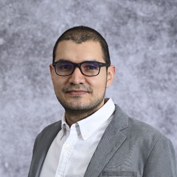 A man wearing glasses in front of a grey backdrop