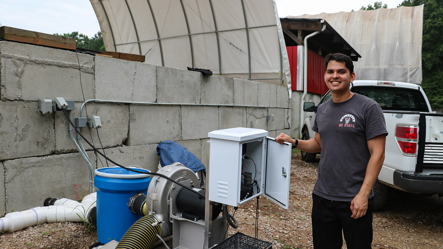 a man stands next to an electrical components box and a pump systems adjacent to a covered pile of compost
